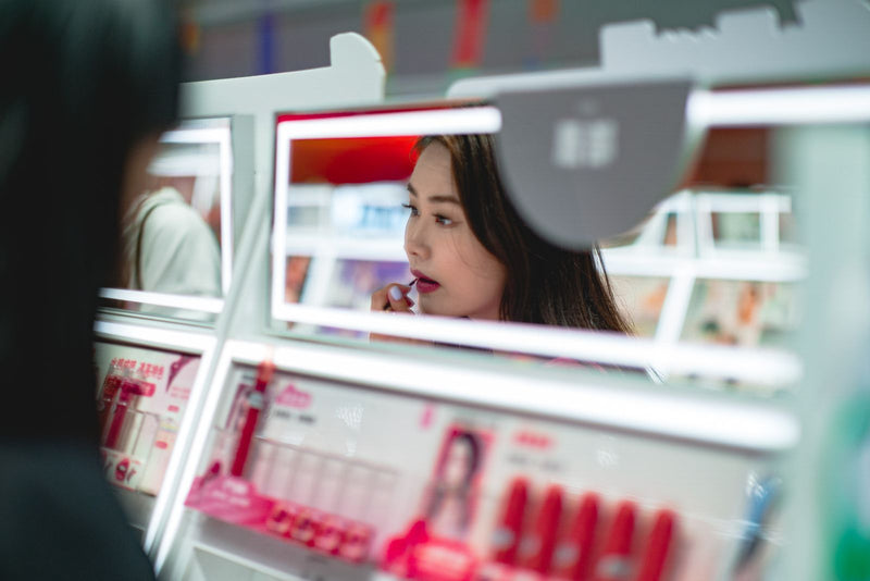 Young woman testing a shade in the mirror of a glowing cosmetics counter.