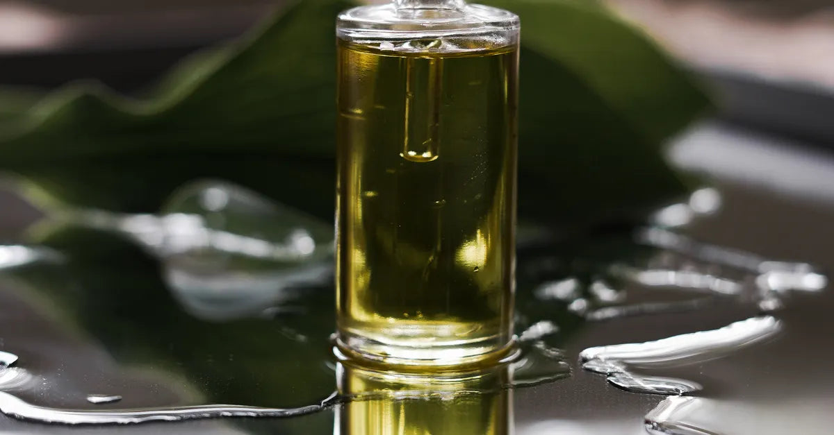 Golden botanical oil in a glass vessel on wet tropical leaves